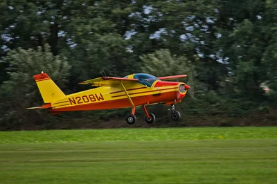 A vibrant small airplane taking off from a manicured grass runway surrounded by lush green trees, representing the fly-in resort experience at Gaston's.