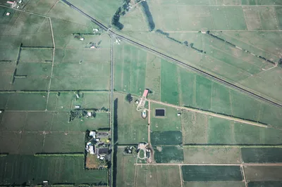 Aerial shot showcasing expansive green farmland with field boundaries and rural structures.