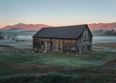 A rustic barn set against the misty Adirondack mountains at sunrise in Upstate New York.