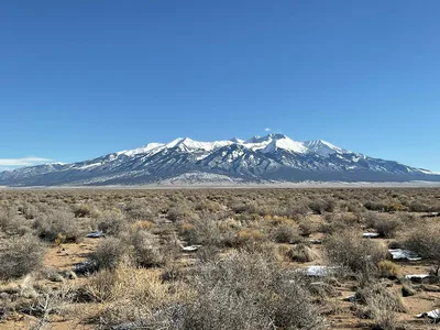 Aerial-style view of a wide dry grass field leading toward snowcapped mountains in Alamosa, Colorado