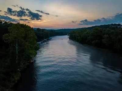 Aerial view of a serene river with lush trees at sunrise in Hollister, Missouri, near Branson Airport.