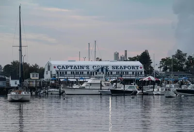 Serene view of Captain's Cove Seaport at sunset with various boats docked, reflecting on calm waters.