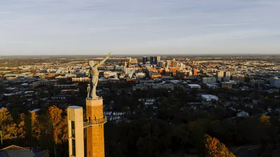 Aerial drone view of the Vulcan statue overlooking the Birmingham, Alabama skyline at sunset.
