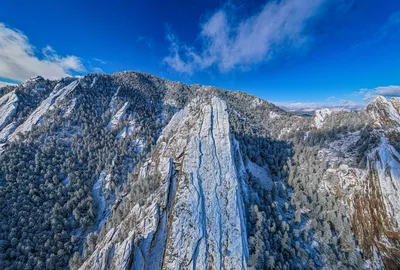 Breathtaking aerial view of the snow-covered Flatirons in Boulder, Colorado, under a clear blue sky.