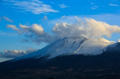 Mesmerizing view of Mount Asama with snow, clouds, and blue sky, creating a picturesque landscape.