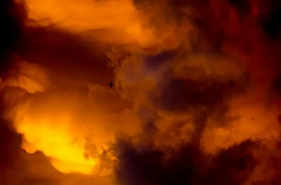 An airplane silhouette flying through dramatic orange storm clouds at sunset in Burlington, WI.