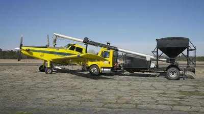 A yellow crop duster airplane being loaded with equipment on the tarmac under a clear blue sky