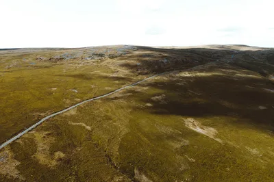 Aerial photograph capturing a remote road cutting through expansive grassland under a bright sky.