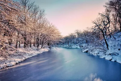 A stunning aerial view of a frozen river surrounded by snowy trees at sunset in Eureka, Kansas.