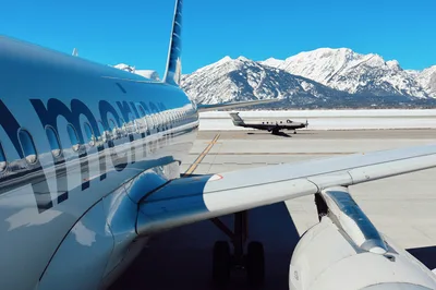 General aviation airplanes parked on the ramp at Jackson Hole Airport (KJAC) with the snow-covered Teton Range in the background.