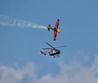 Dynamic aerobatic display with Red Bull aircraft and helicopter in Oshkosh sky.