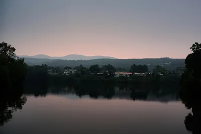 A serene twilight view of a river reflecting a small town skyline and distant mountains