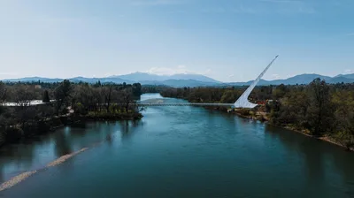 Aerial view of the iconic Sundial Bridge over the Sacramento River in Redding, California, with snow-capped mountains in the background.