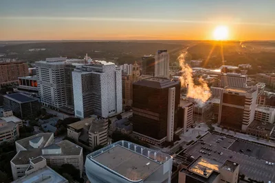 Aerial sunrise view of the Rochester, MN skyline, featuring the city's urban architecture and a vibrant sun flare.