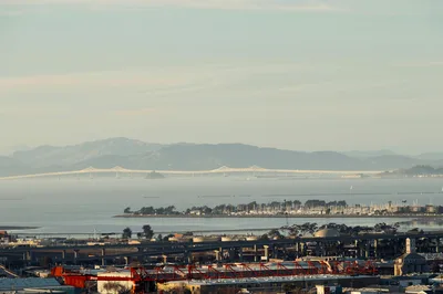 Aerial view of the San Francisco Bay waterfront with industrial areas and distant mountains.