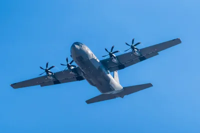 A Lockheed C-130 Hercules military aircraft in flight against a clear blue sky.