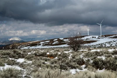 Wind turbines on snowy hills in Tehachapi, California, under a dramatic mountain sky.