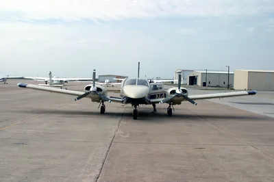 A Piper Seminole twin-engine aircraft on a sun-drenched Texas tarmac, with hangars in the background.